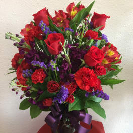 Bouquet of red roses, carnations, and purple filler in a glass vase