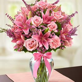 Pink roses and lilies arranged in a clear glass vase with a pink ribbon