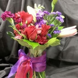 Mixed bouquet of red roses, lilies, and purple flowers in a glass vase