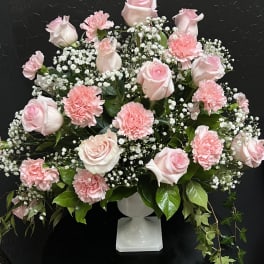 Pink roses and carnations arranged in a white pedestal vase