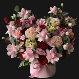 Pink and red mixed flower arrangement in a round box