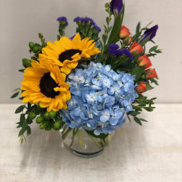Bouquet of sunflowers, blue hydrangea, and orange roses in a glass vase
