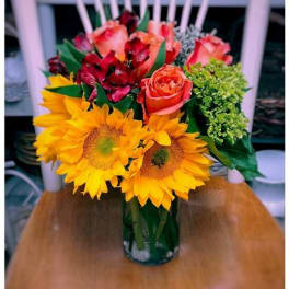 Bouquet of sunflowers, roses, and red alstroemeria in a glass vase
