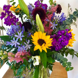 Mixed bouquet with sunflowers, lilies, and purple blooms in a glass vase