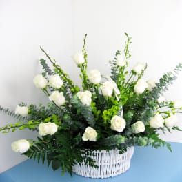 White roses arranged in a white wicker basket with greenery