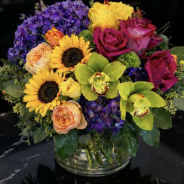 Colorful bouquet with roses, sunflowers, orchids, and hydrangeas in a glass vase