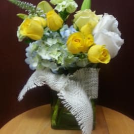 Yellow roses and pale blue hydrangeas in a glass vase with burlap ribbon