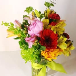 Colorful bouquet of mixed flowers in a clear glass vase with a lime ribbon