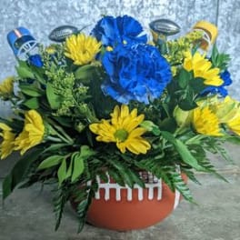 Blue and yellow floral arrangement in a football-shaped container