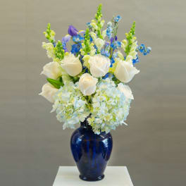 White roses and blue flowers arranged in a cobalt vase