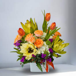 Orange tulips and roses in a white vase with purple accents