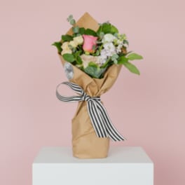 Wrapped bouquet of pink and cream roses with a striped ribbon