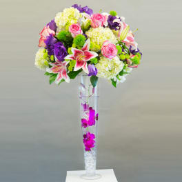 Tall bouquet of pink roses, lilies, and purple flowers in a clear vase