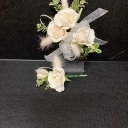 White rose corsage and boutonniere with ribbon on a dark background