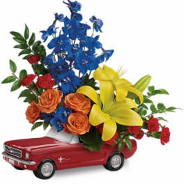 Flower arrangement in a red toy car with blue, orange, and yellow blooms