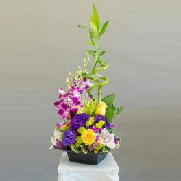 Tall floral arrangement with purple, yellow, and white blooms in a black container