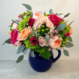 Mixed bouquet of pink, peach, and green flowers in a blue pitcher vase