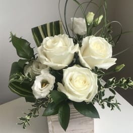 White roses and lisianthus in a square wooden vase with looping grass accents