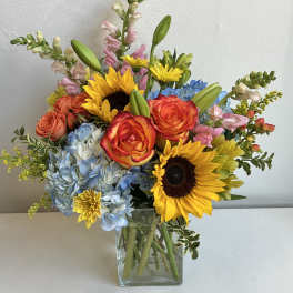 Mixed bouquet with sunflowers, roses, hydrangeas, and snapdragons in a glass vase