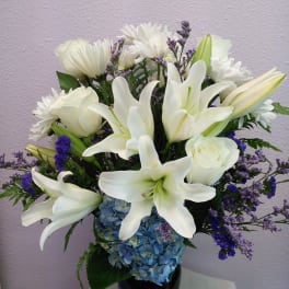 White lilies and roses in a black vase with blue hydrangeas and purple filler