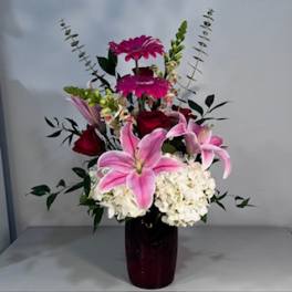 Pink lilies and red roses in a dark vase with white hydrangeas