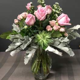 Pink roses arranged in a clear glass vase with silver foliage and a green succulent