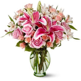 Pink lilies and roses arranged in a clear glass vase