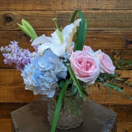 Pink roses, blue hydrangea, and a white lily in a glass vase