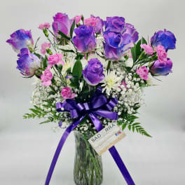 Purple roses and pink carnations in a glass vase with a purple ribbon