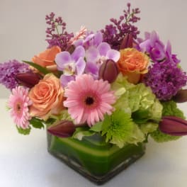 Mixed bouquet in a square glass vase with pink, purple, and orange flowers