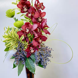 Tall arrangement of red orchids in a dark vase with green accents