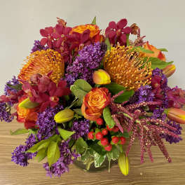 Bright mixed bouquet with orange roses, purple blooms, and yellow tulips in a glass vase