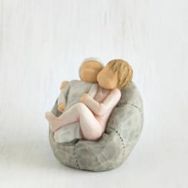 Two small child figurines sitting together on a gray stone-like base
