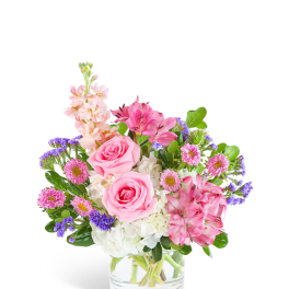 Short glass vase arrangement with pink roses, white hydrangeas, and mixed pink and purple flowers.