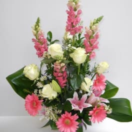 Tall arrangement of pink snapdragons, gerbera daisies, lilies, and white roses in a purple pot