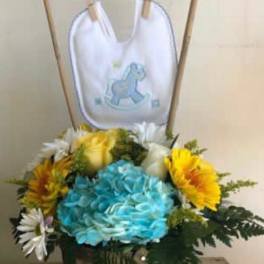 Colorful flower arrangement in a wooden basket with a baby bib on sticks