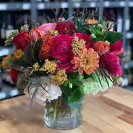Mixed bouquet of pink, orange, red, and white flowers in a clear glass vase