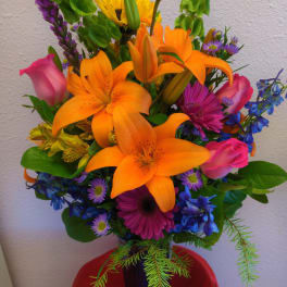 Colorful bouquet with orange lilies, pink roses, and purple flowers in a vase