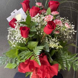 Red roses and pink carnations in a glass vase with a red ribbon