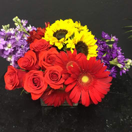 Red roses with yellow sunflowers and purple flowers in a low arrangement