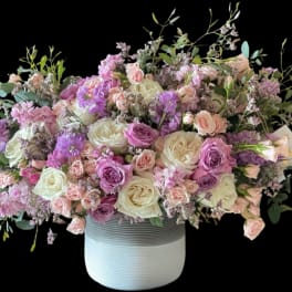 Large pastel bouquet of roses and purple flowers in a white vase