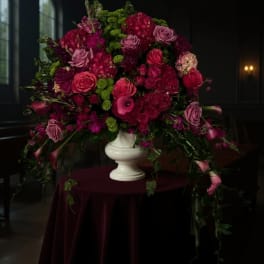 Large magenta and pink floral arrangement in a white urn vase