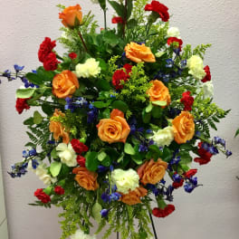 Large standing floral spray with orange roses, red carnations, and white blooms