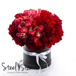 Red roses and pink orchids arranged in a black hat box
