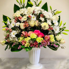 Tall mixed arrangement of white daisies, roses, lilies and pink flowers in a white pedestal vase