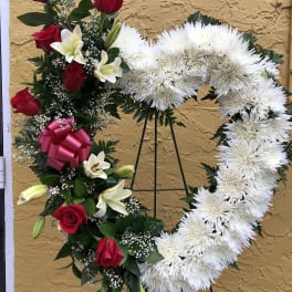 Tall heart-shaped white wreath with red roses and white lilies on a metal easel stand