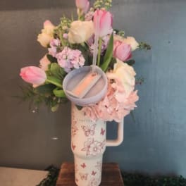 Pastel pink and white flower arrangement in a printed travel tumbler with a small candle on a wooden stand