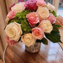 Compact arrangement of pink and white roses with green blooms in a patterned ceramic vase