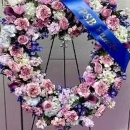 Large floral wreath of pink, white, and purple flowers on a stand with a blue ribbon
