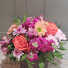 Low arrangement of orange roses, pink mums, and peach gerberas in a wooden box